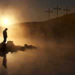 Sillouette of a person with a bowed head before the cross